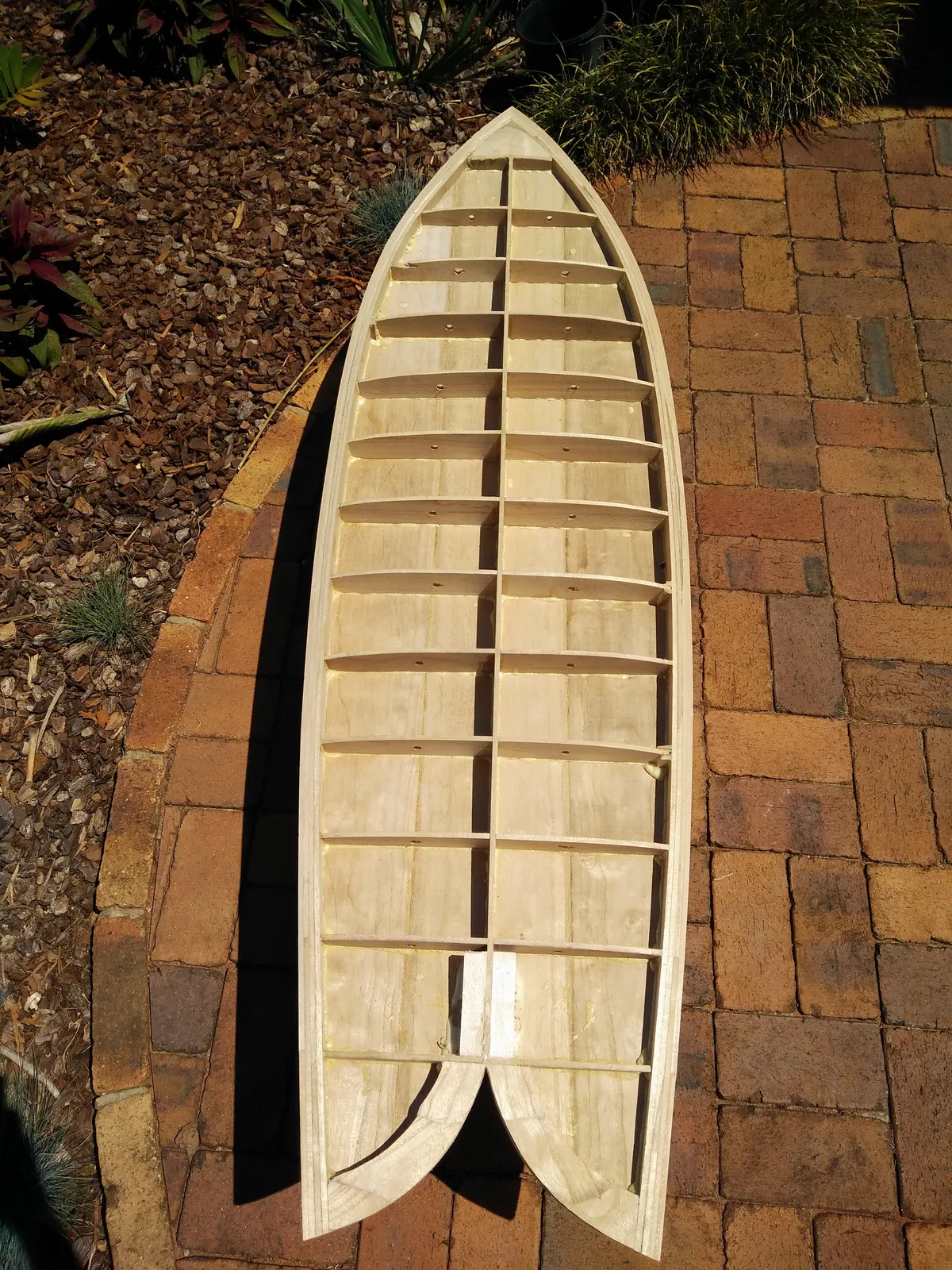 Top-down view of a hollow wooden surfboard frame showing spine, ribs and swallow-tail blocks before skinning