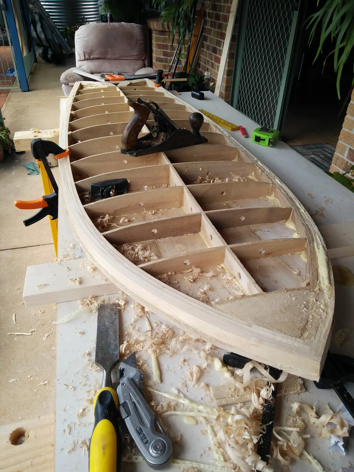 Laminated timber rail strips clamped around a hollow wooden surfboard frame with hand planes on the deck